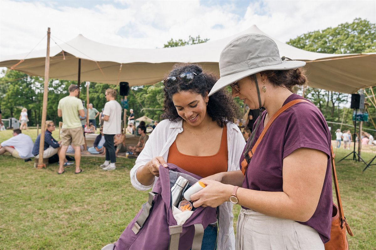 Twee vriendinnen controleren water, zonnebrand en oordoppen in hun tas op een zomers evenement
